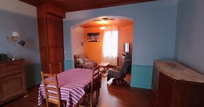 A cozy room with a dining table, chairs, a television, and a wooden cabinet. - Village House with Courtyard near Issoire (Perrier)