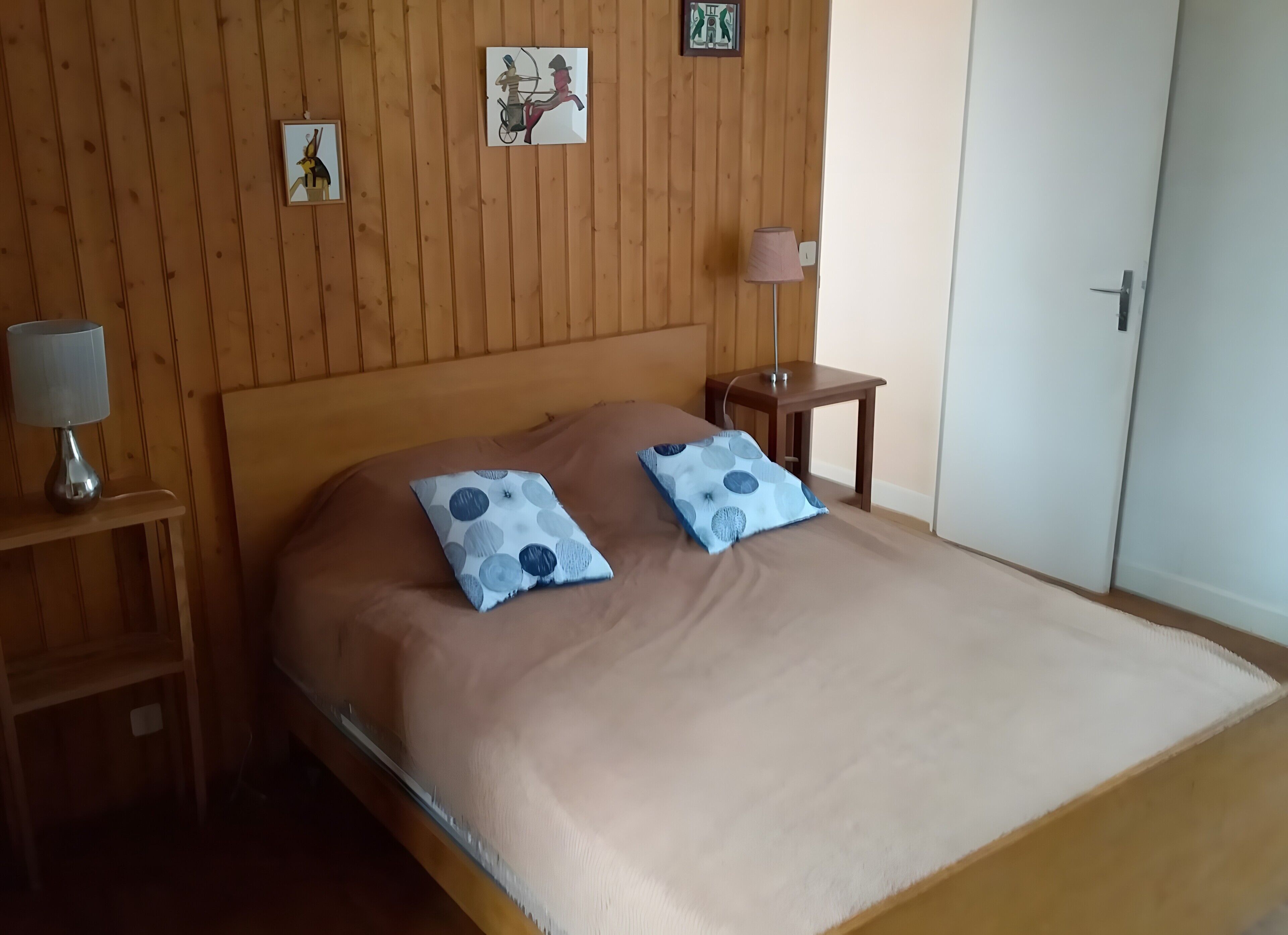 Een netjes opgemaakt bed met twee kussens, een bedlampje en een klein houten nachtkastje.