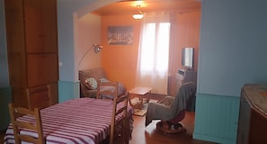 A compact room with a bed, a chair, a small table, a television, and a painting on the wall.