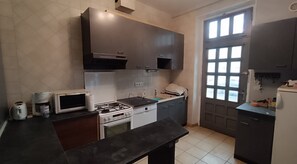 A kitchen with a gas stove, microwave, oven, and a window with blinds.
