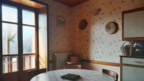 Une pièce avec une table ronde, des chaises, un radiateur, un mur orné d’un motif floral et une fenêtre avec des stores.