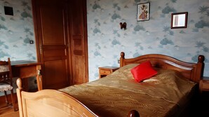 Un lit en bois avec un oreiller rouge, une table de chevet et un mur orné d’un motif floral.