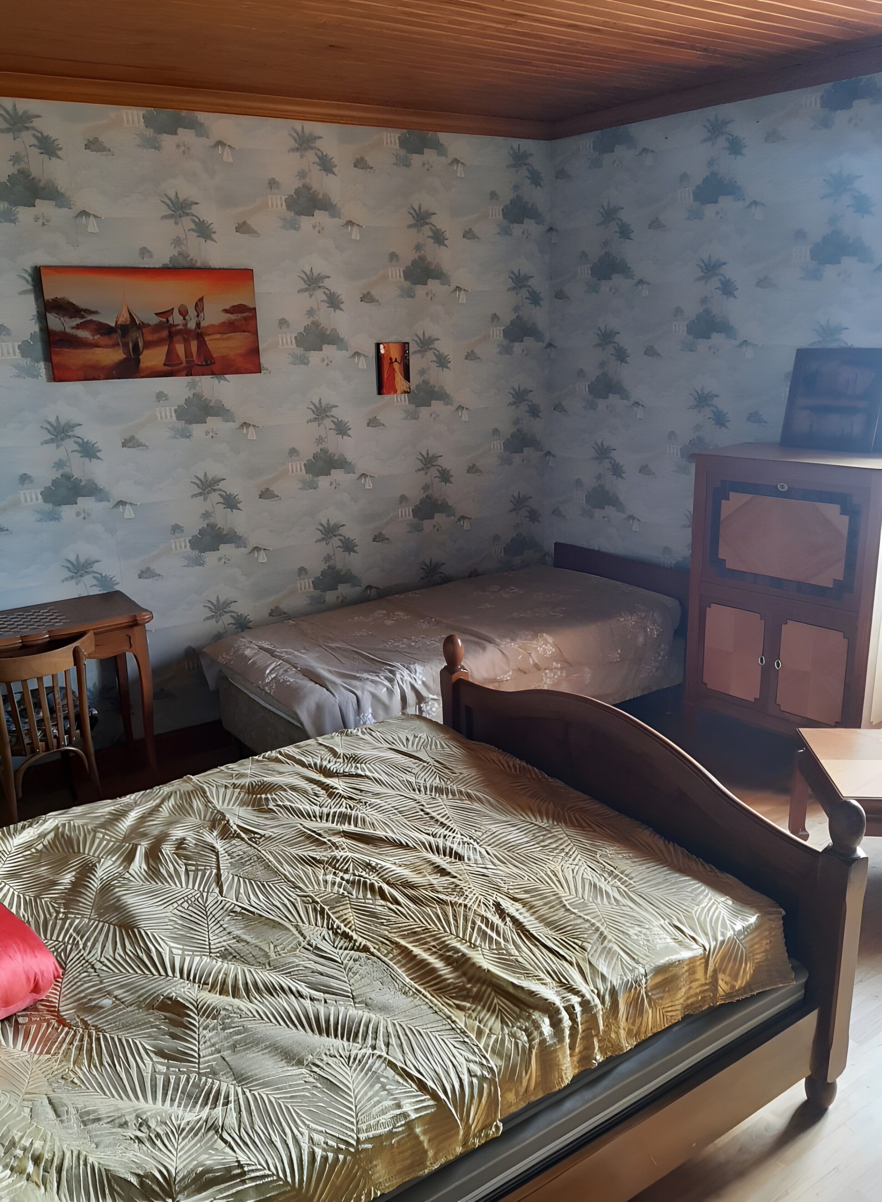Una habitación con dos camas, un escritorio de madera, un armario y papel tapiz estampado.