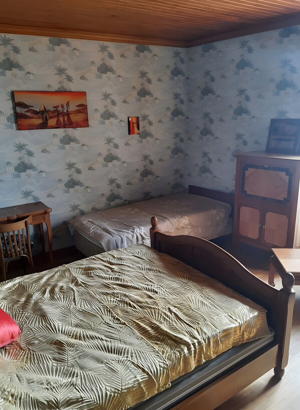 A room with two beds, a wooden desk, a cabinet, and patterned wallpaper.
