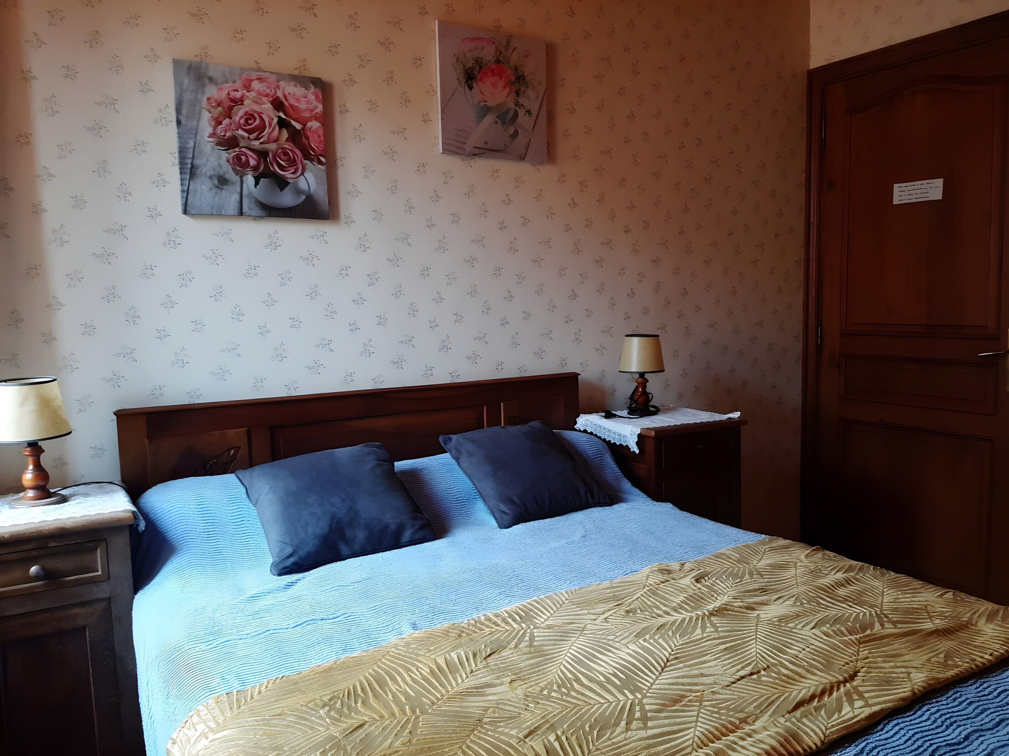 Ein Schlafzimmer mit einem Bett, zwei Nachttischen, einer Holztür und blumigem Wandpapier.