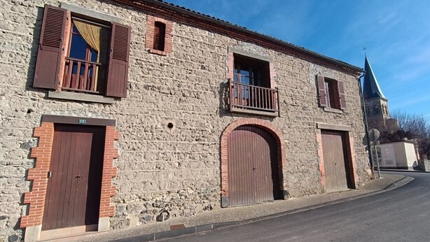 Un bâtiment en pierre doté d’une grande entrée en arc de cercle, d’un petit balcon et d’un clocher.