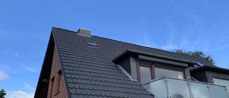 Un edificio residencial con techo inclinado, un tragaluz en el ático y un balcón con barandilla de vidrio.