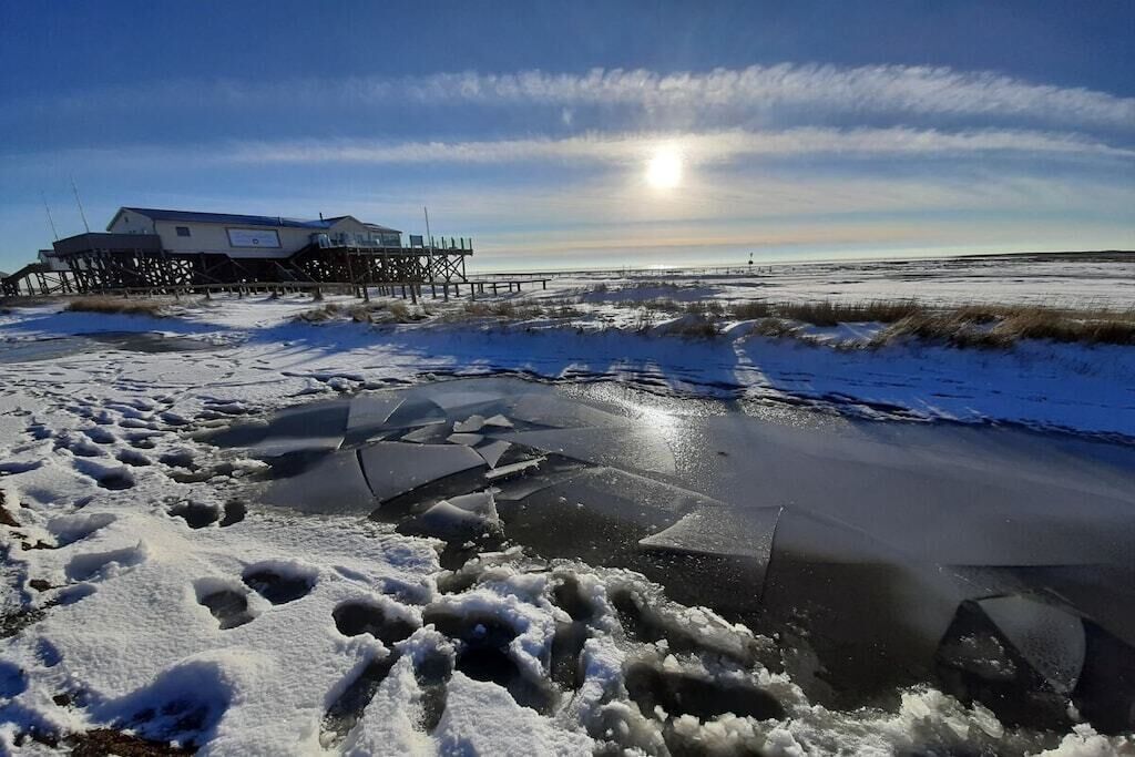 A building on stilts over a frozen body of water with a clear sky.
