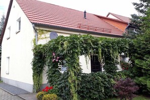 Ein Haus mit rotem Ziegeldach, Efeu bewachsene Wände und einem Fenster mit kreisförmigem Design.