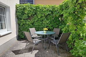 Eine Terrasse mit einem runden Tisch und vier Stühlen, umgeben von üppigem Grün.
