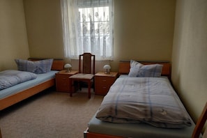 Ein Schlafzimmer mit zwei Einzelbetten, einem Holzstuhl, einem kleinen Tisch und einem Fenster mit durchsichtigen Vorhängen.