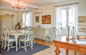 Een eetgedeelte met een ronde tafel, stoelen, een kroonluchter en een kast.
