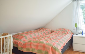 Ein Schlafzimmer mit schrägverdeckter Decke, einem Bett mit gemustertem Überwurf, einem Nachttisch mit Lampe und einem Fenster mit Vorhängen.