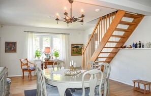 Ein Essbereich mit einem runden Tisch, weißen Stühlen, einer Chandelüstere und einer Holztreppe.