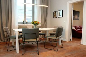A dining area with a white table and four chairs, a vase with flowers, and a red couch in the background. - Erbschulzenhof (Müritz) 6 Pers. (Buchholz (Müritz))