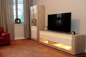 Ein modernes Wohnzimmer mit einem Flachbildfernseher auf einem Holzboden, einem roten Sofa und einem Fenster mit Vorhängen.