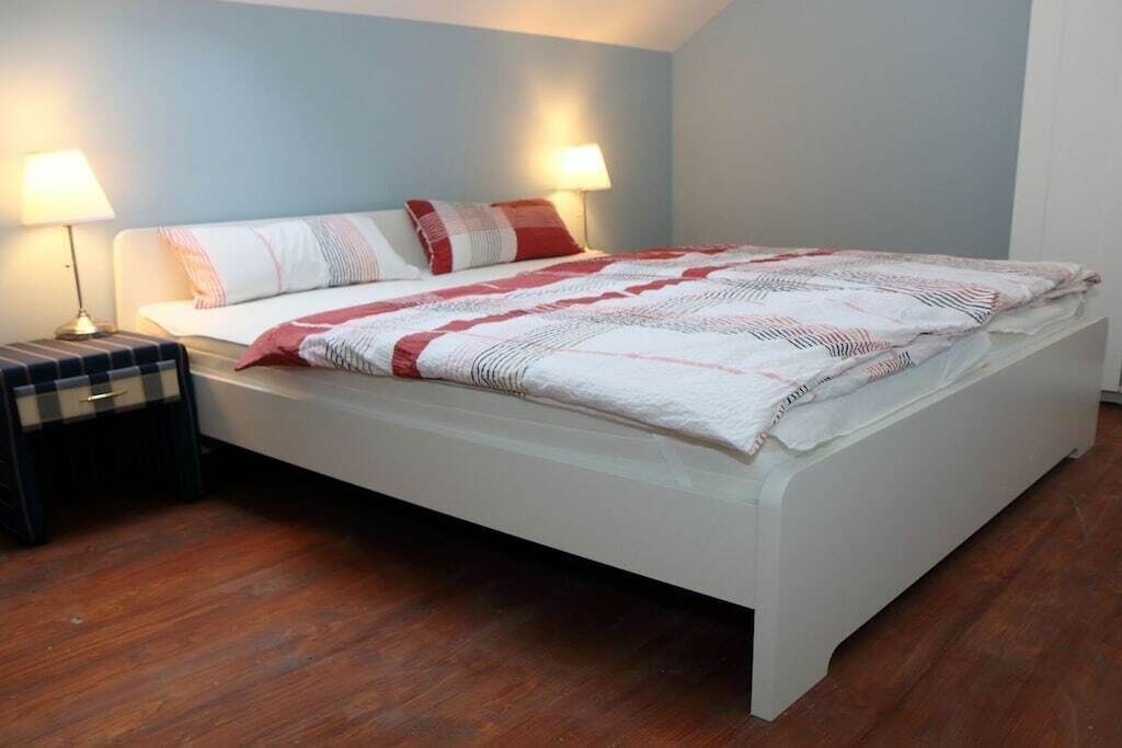 Un letto rifatto con una testiera bianca, due lampade ai comodini e un comodino a quadri.