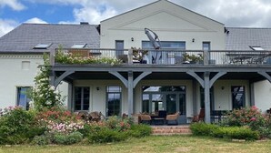 Uma casa de dois andares com varanda coberta, garagem e jardim com plantas floridas.