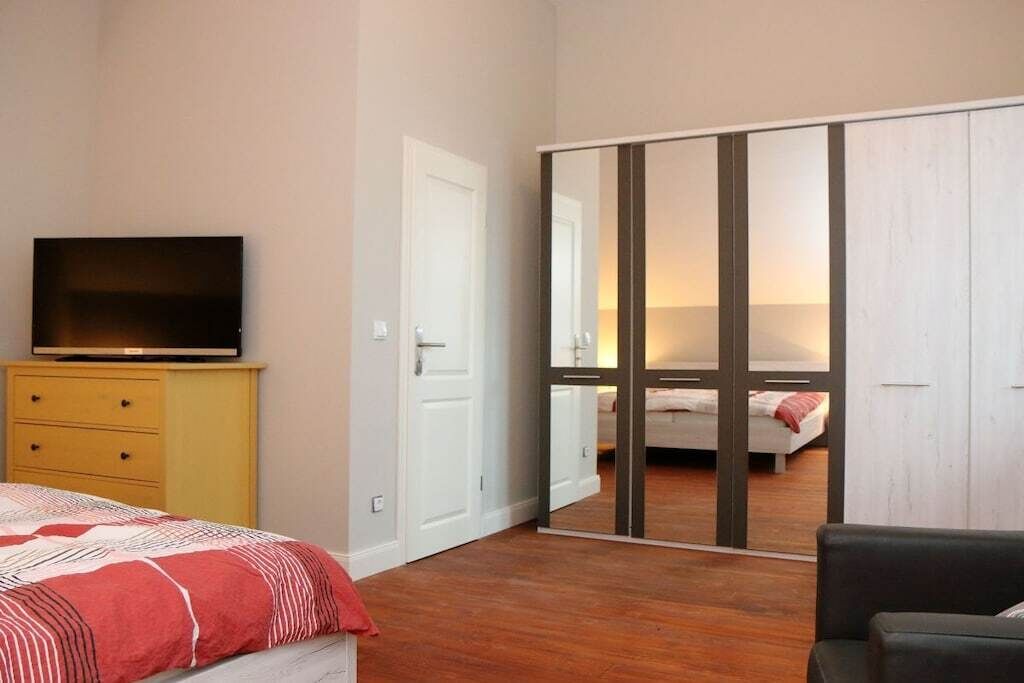 Une chambre à coucher avec un lit, un téléviseur posé sur une commode, une armoire et un miroir qui reflète la pièce.