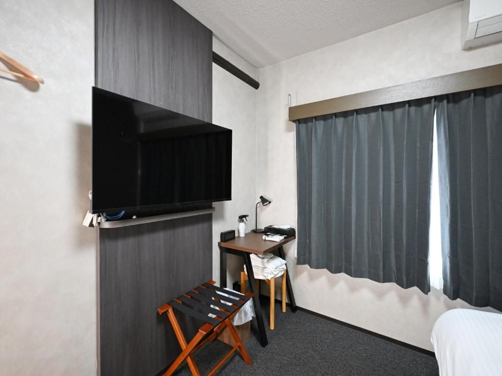 A hotel room with a bed, a desk, a chair, a television, and a window with curtains.