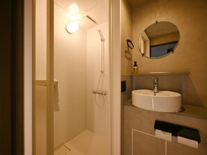 Un baño con ducha, lavamanos, espejo y perchero para toallas.