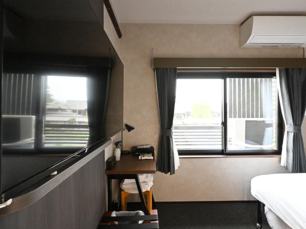 Habitación de hotel con cama, escritorio, silla, ventana con cortinas y equipo de aire acondicionado.