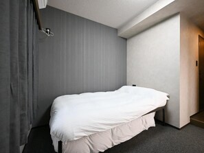 Una cama individual en una habitación con pared gris y una puerta a la derecha.