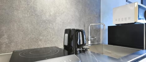 Une cuisine Ă©quipĂ©e dâune plaque de cuisson Ă induction moderne, dâune bouilloire et dâun four Ă micro-ondes, le tout installĂ© sur un plan de travail en acier inoxydable.