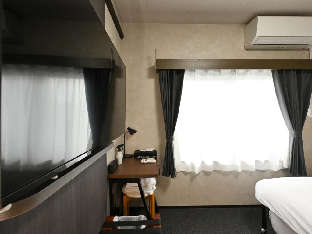 A hotel room with a bed, a desk, a chair, a lamp, and a window with curtains.
