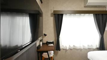 A hotel room with a bed, a desk, a chair, a lamp, and a window with curtains.