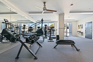 Ein modernes Fitnessstudio mit unterschiedlichen Trainingsgeräten, großen Fenstern und einem Deckenventilator.