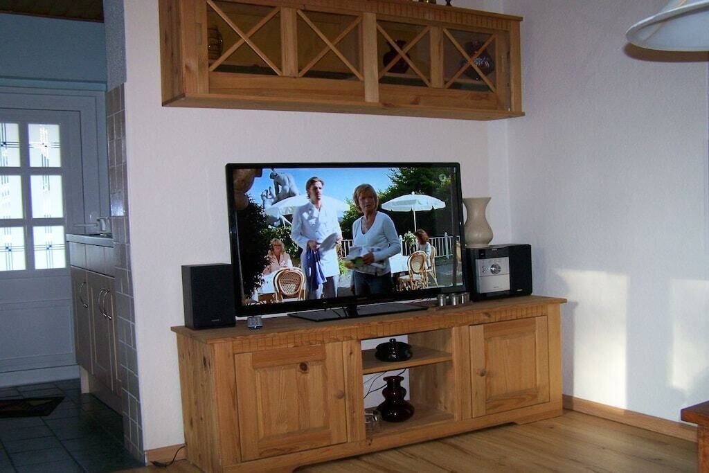 A television on a wooden stand with a cabinet below it, a vase, and a small table with a lamp.