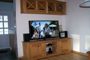Ein Fernseher auf einem Holzboden mit einem Schrank darunter, eine Vase und ein kleiner Tisch mit einer Lampe.