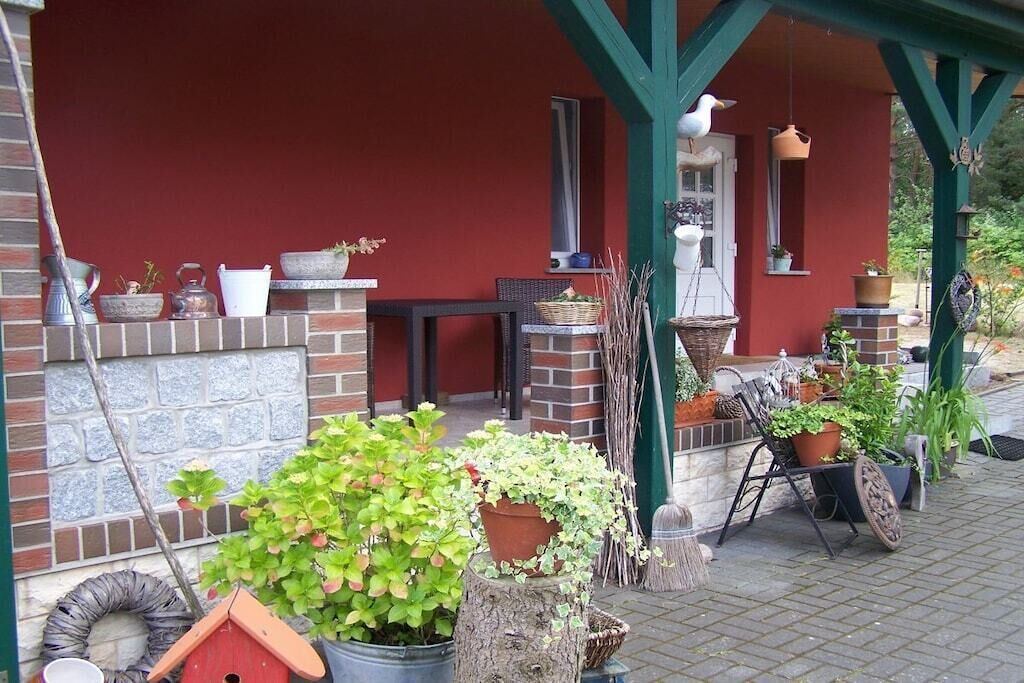A covered porch with potted plants, a birdhouse, and outdoor furniture.