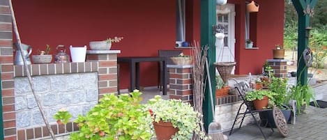 A covered porch with potted plants, a birdhouse, and outdoor furniture.