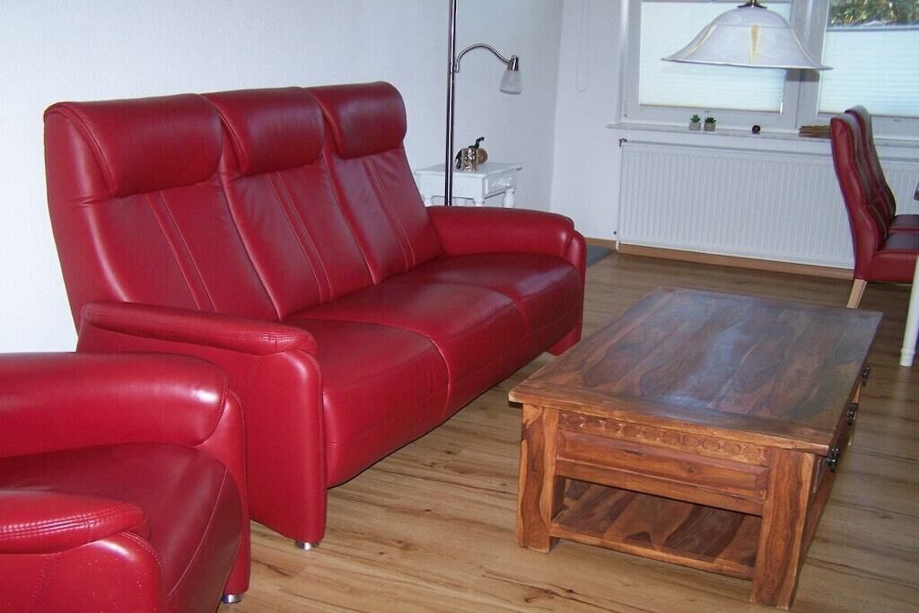 En röd lädersoffa, ett träbord och en lampa i ett rum med trägolv och vita väggar.