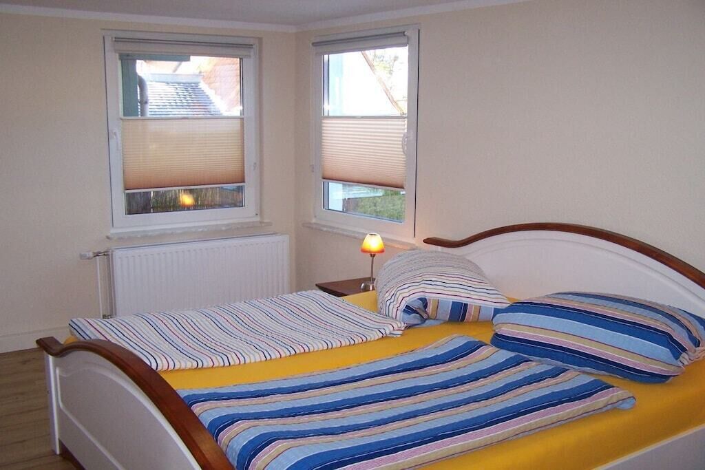 A bedroom with a bed, two windows with blinds, a bedside lamp, and a radiator.