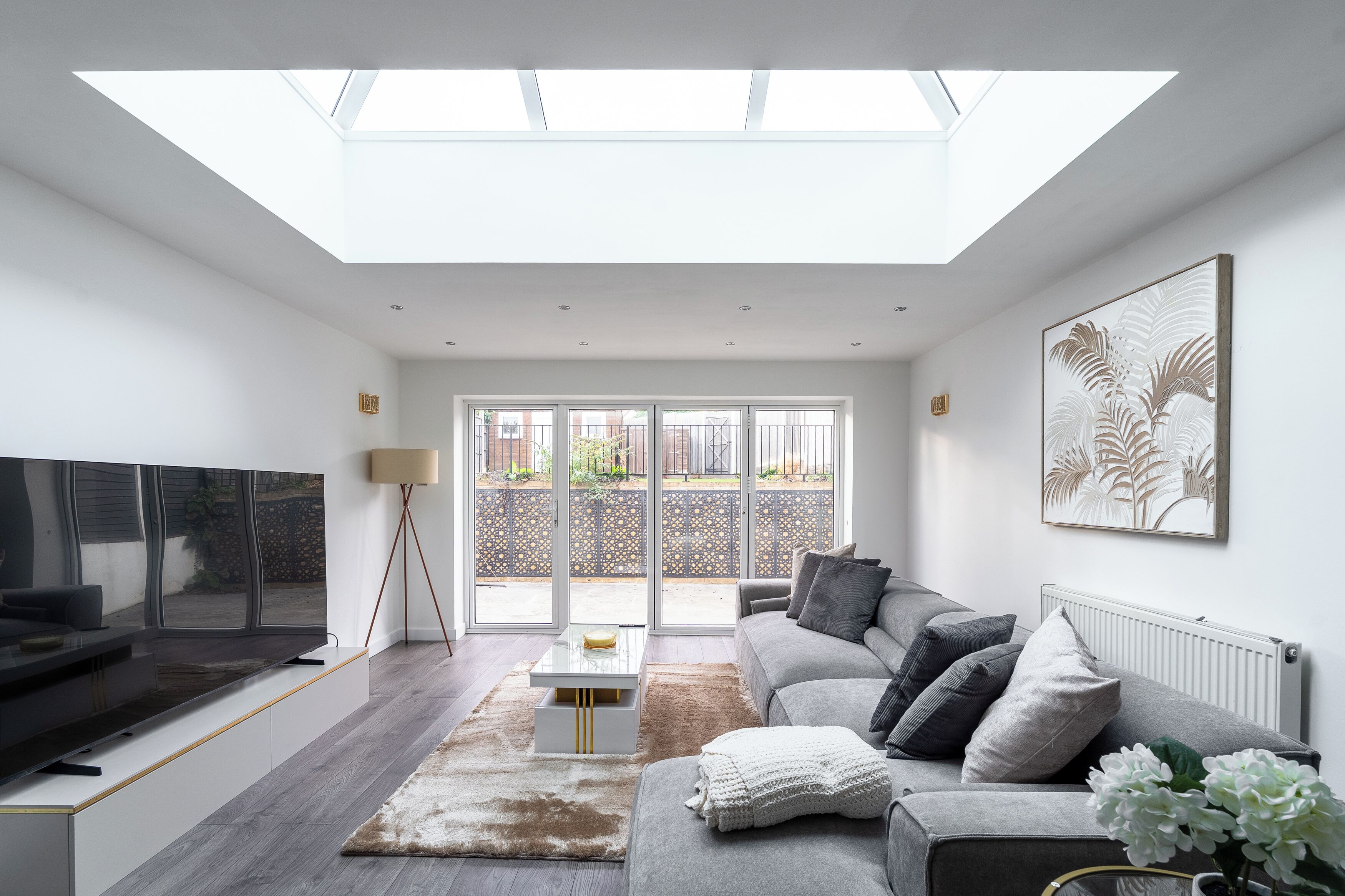 A modern living room with a flat-screen TV, a sofa, a coffee table, and a large window with a view of the outside.