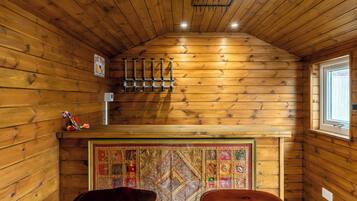 A wooden interior with a sloped ceiling, a hanging light fixture, a bar area with stools, and a decorative wall panel.