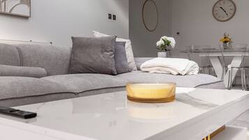 A modern living room with a sofa, a coffee table, and a dining area in the background.
