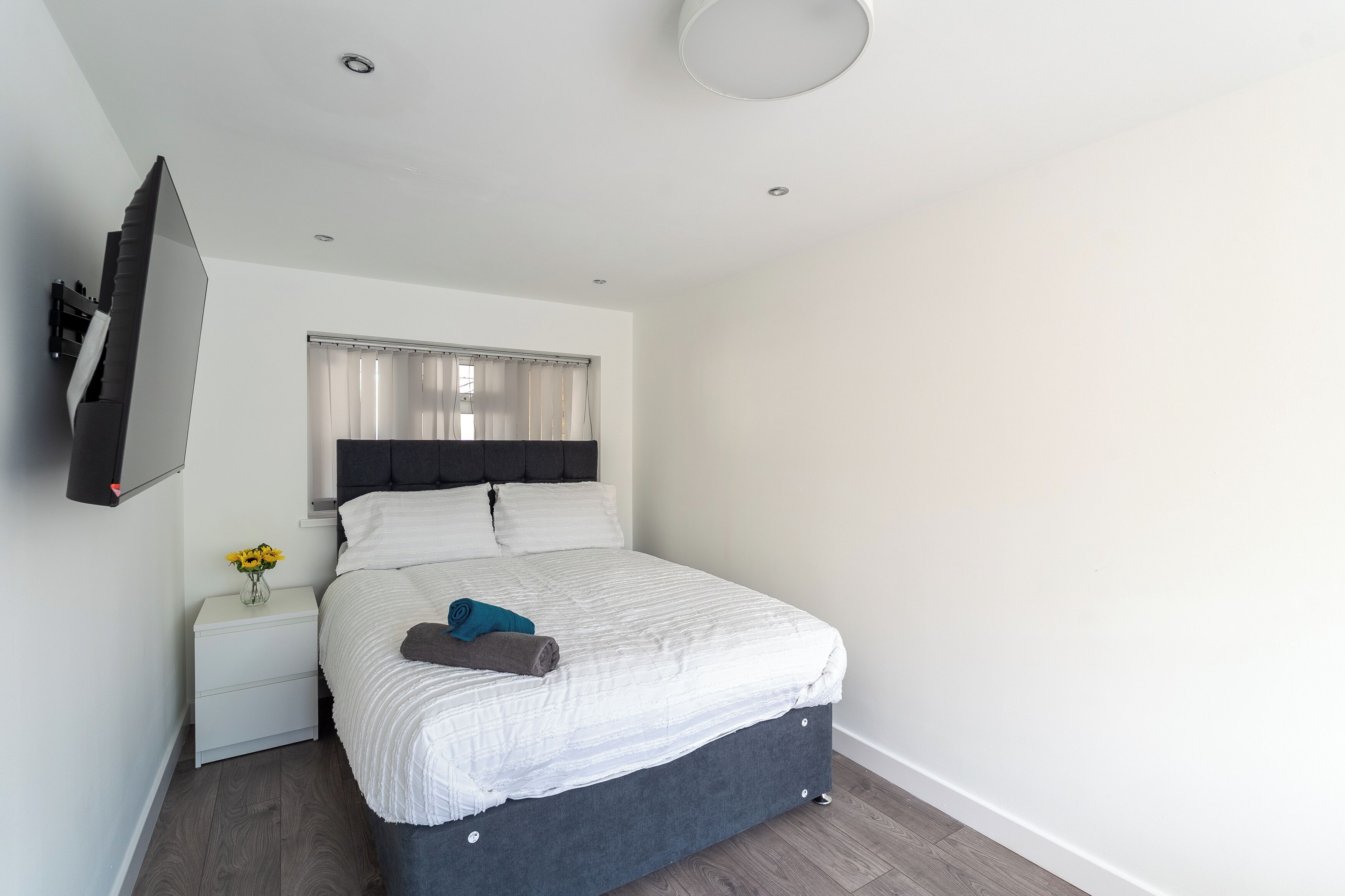 A modern bedroom with a bed, a nightstand, a TV mounted on the wall, and a window with curtains.