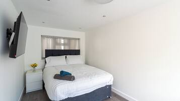 A modern bedroom with a bed, a nightstand, a TV mounted on the wall, and a window with curtains.