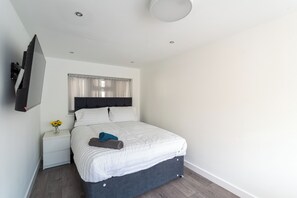 A modern bedroom with a bed, a nightstand, a TV mounted on the wall, and a window with curtains. - 4 bedroom home in Croydon (Croydon)