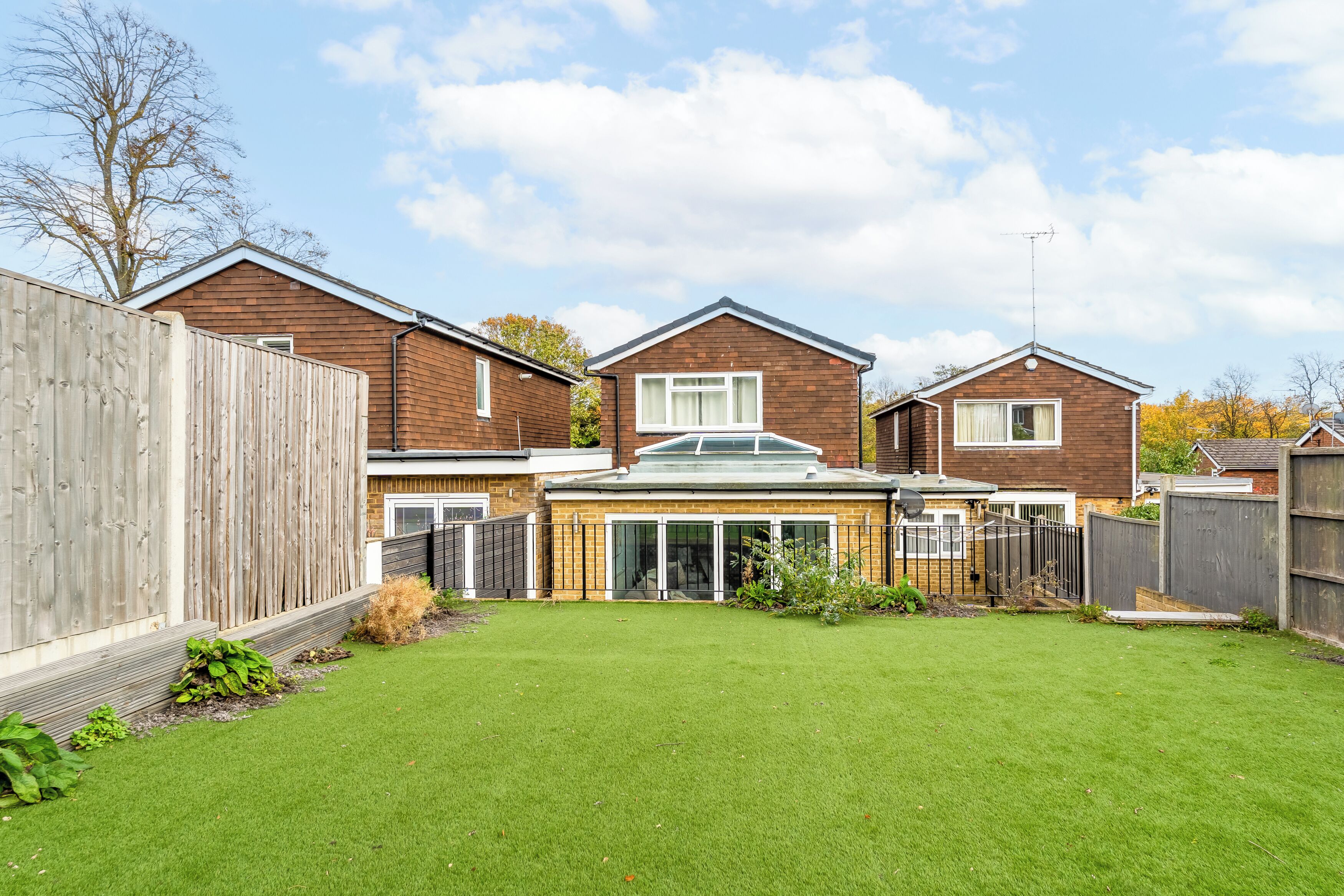 A residential area with three houses, a fenced backyard, and a clear sky.