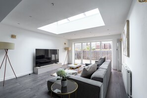 A modern living room with a flat-screen TV, sofa, coffee table, and a skylight. - 4 bedroom home in Croydon (Croydon)