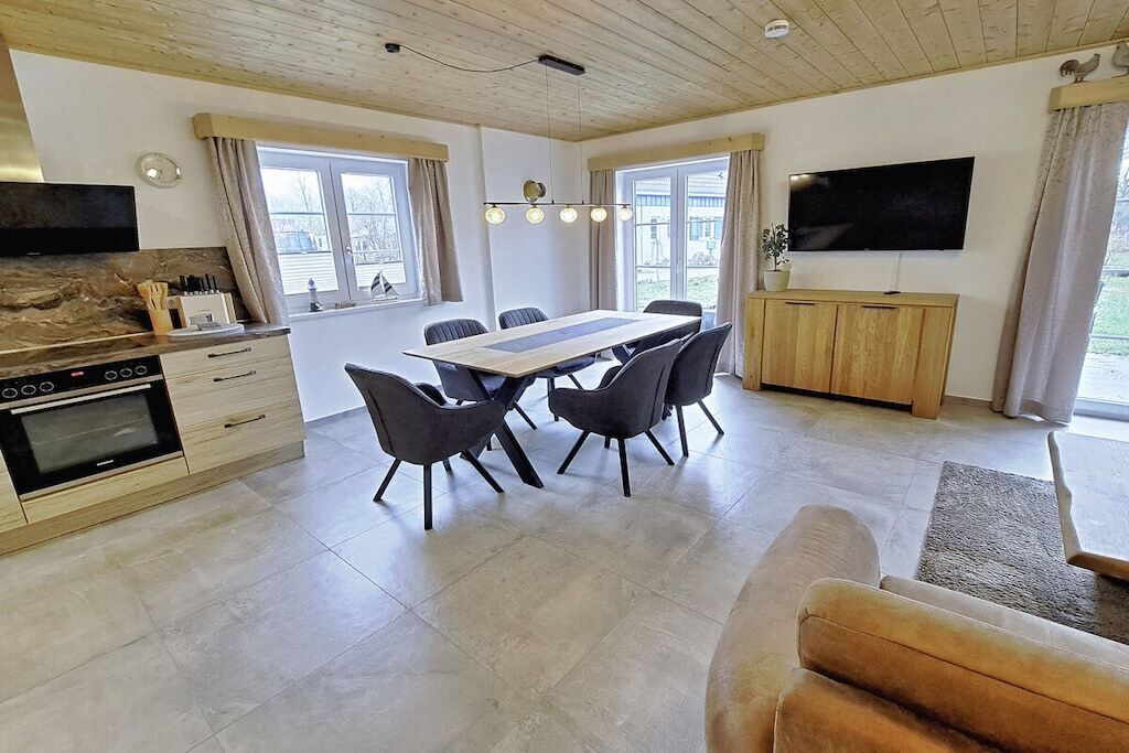 A modern kitchen with a dining area, a flat-screen TV, and a large window.