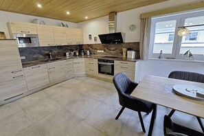 A modern kitchen with wooden cabinets, a built-in microwave, and a dining area with a table and chairs. - Holiday home in Altefähr with swimming pool (Altefähr)