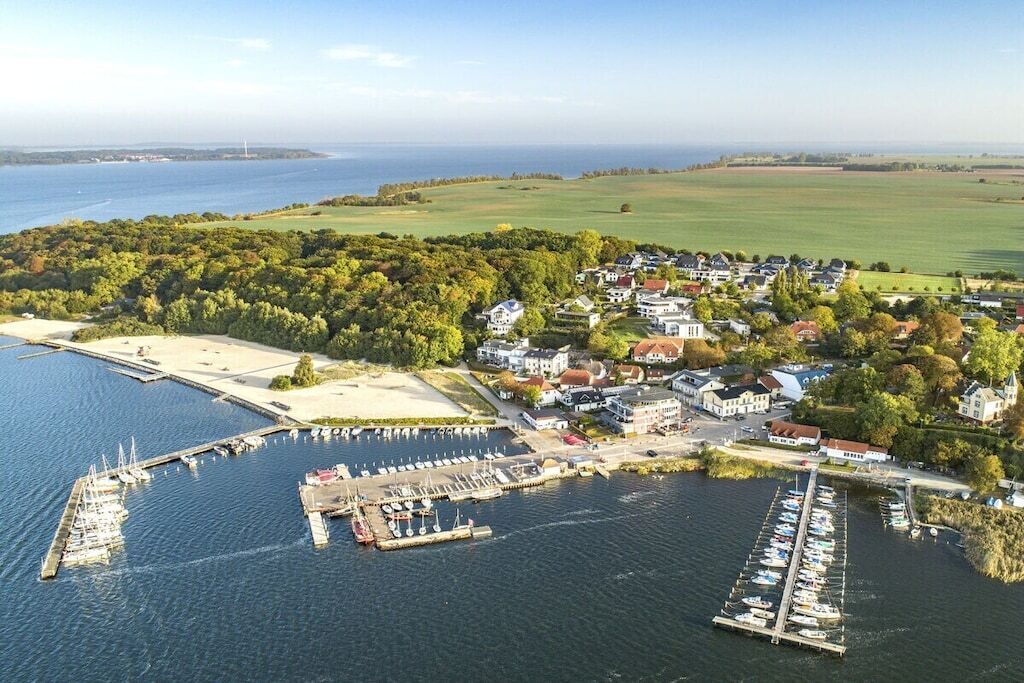 An aerial view of a coastal village with a marina, houses, and a lighthouse in the distance.