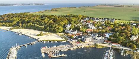 An aerial view of a coastal village with a marina, houses, and a lighthouse in the distance.