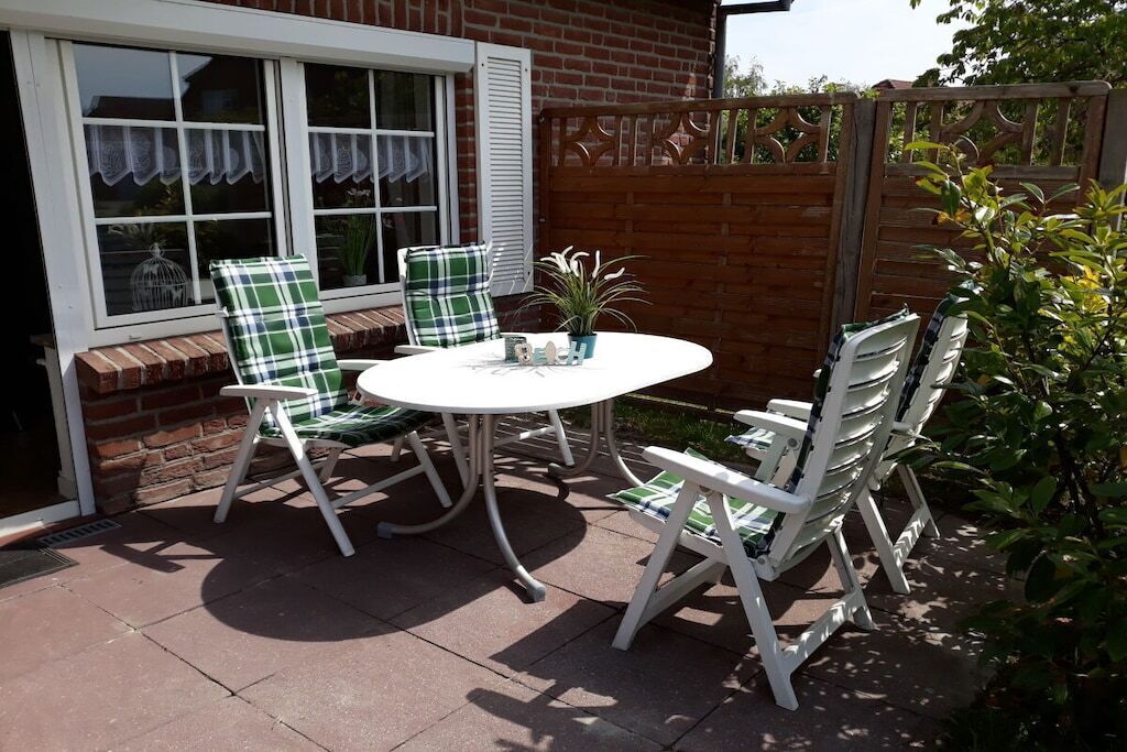 An outdoor patio with a round table and four white chairs with green and white checkered cushions.